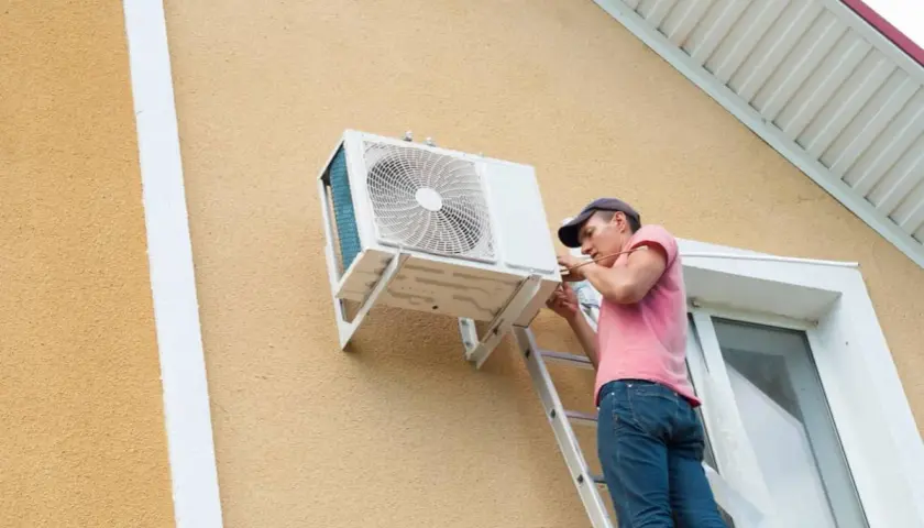Técnico en escalera realizando la **instalación aire acondicionado exterior** en la pared de una casa.