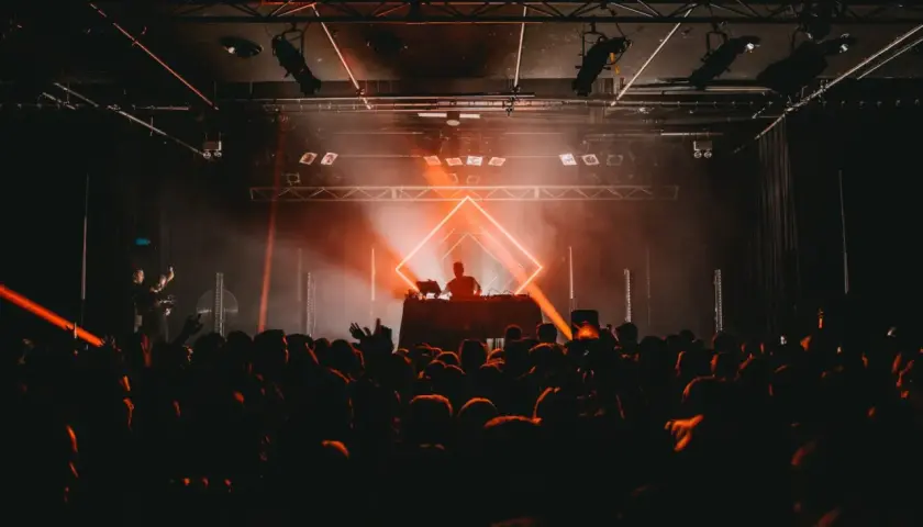 DJ set sous un éclairage orange vif, ambiance techno année 90. Foule en délire devant la scène.