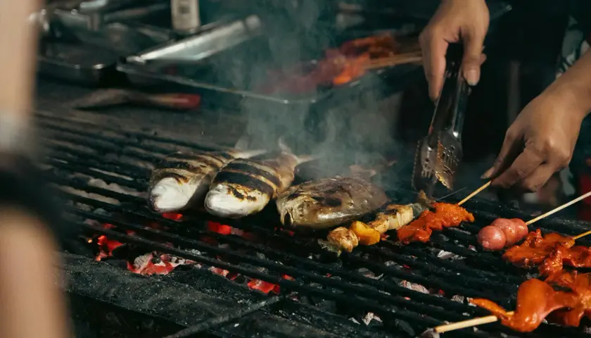 Poissons et brochettes marinés cuisent sur un gril incandescent, dégageant une fumée alléchante. Un vrai bar au barbecue !