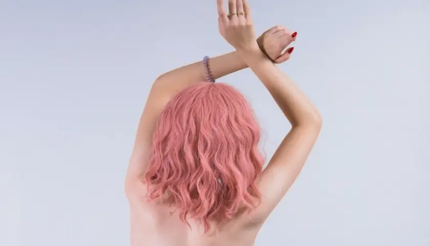 Kobieta z falowanymi włosami w odcieniu kolor magenta, z rękami skrzyżowanymi nad głową.