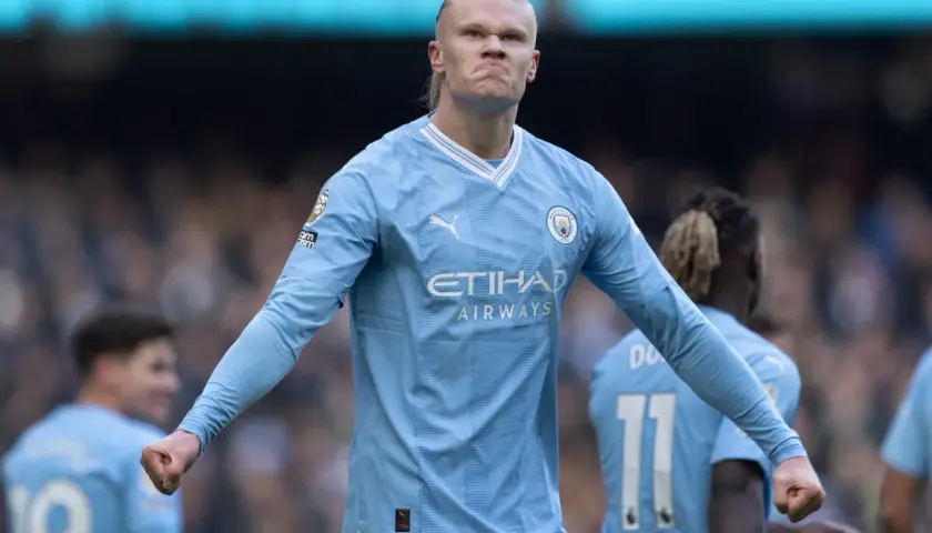 Erling Haaland, najdroższy piłkarz świata, w błękitnej koszulce Manchesteru City, z zaciętą miną i zaciśniętą pięścią.