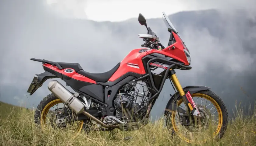 Rieju Aventura 500, lista para la aventura. Ficha técnica de esta moto trail roja y negra en un paisaje montañoso.