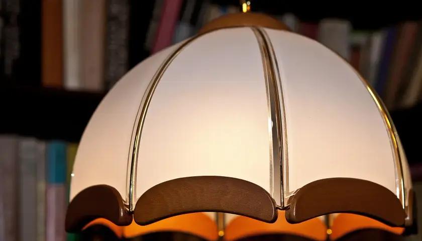 Jak wyczyścić abażur z materiału? Delikatne czyszczenie lampy wiszącej z białego materiału i drewna, na tle regału z książkami.