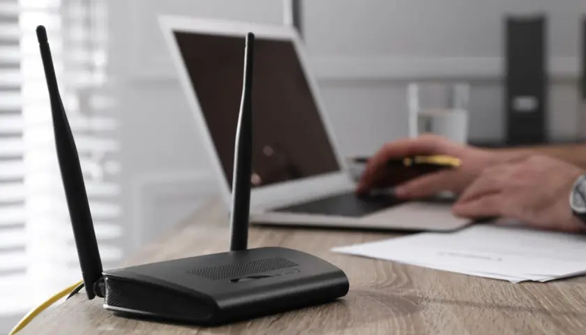 Router mit Antennen steht auf einem Holztisch. Ein Laptop hat kein WLAN mehr, der Nutzer versucht, das Problem zu lösen.