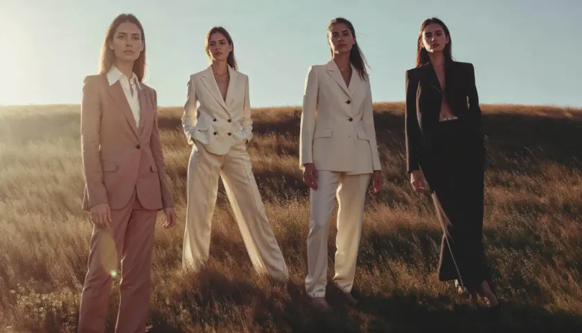 Quatre femmes en tailleurs élégants, dont un en lin textile, posent dans un champ d'herbes hautes au coucher du soleil.