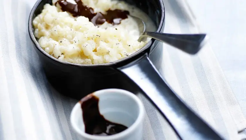 Un délicieux riz au lait au chocolat, servi dans une petite casserole noire, avec une cuillère et un ramequin de sauce chocolat.