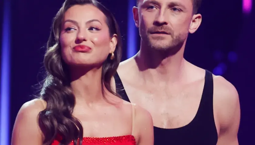 Kamil Nożyński i jego partnerka, w czerwonej sukni i czarnym topie, prezentują się na scenie.