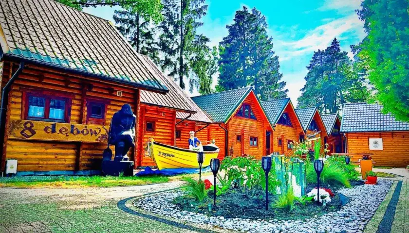 Drewniane domki w lesie, idealne na agroturystykę nad morzem. Obok łódka i rzeźba.