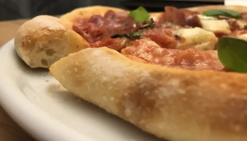 Nahaufnahme einer köstlichen Pizza mit dickem, luftigem Rand, belegt mit Tomaten, Käse und Salami. Ein echter Genuss, wie ein kleiner "pizza canotto".