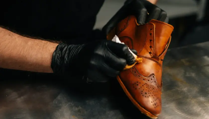 Gants noirs pour un entretien simili cuir. Un homme nettoie une chaussure marron avec un chiffon.