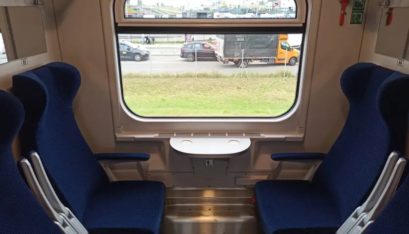 Wnętrze wagonu 174a z niebieskimi siedzeniami i oknem, przez które widać drogę z samochodami i ciężarówką.