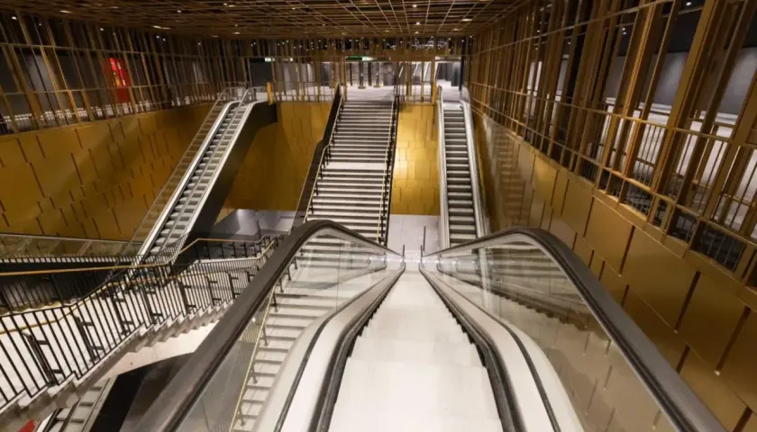 Interno moderno della **metro Cavour Roma**, con scale mobili e gradinate che conducono ai binari, pareti dorate e soffitto a griglia.