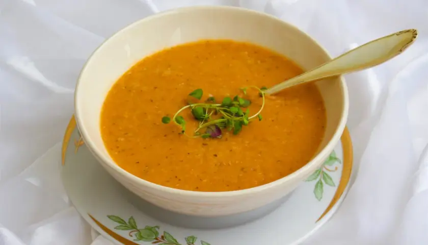 En skål med varm, orange turkisk linssoppa, garnerad med färska örter och en elegant sked.