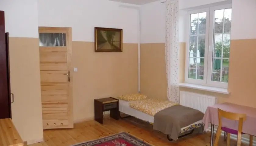 Pokój z łóżkiem, szafką nocną, drzwiami, oknem i dywanem.