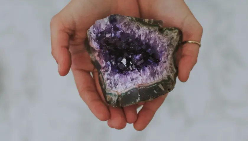 Hände halten einen tiefvioletten Amethyst. Seine Wirkung auf die Haut wird oft als beruhigend beschrieben.