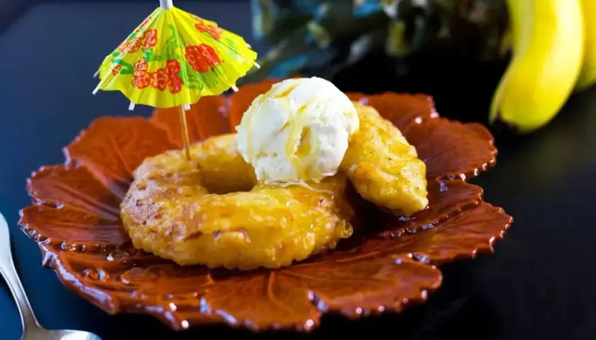 Friterad banan serverad med vaniljglass och en liten gul parasoll. En läcker dessert som påminner om soliga dagar.