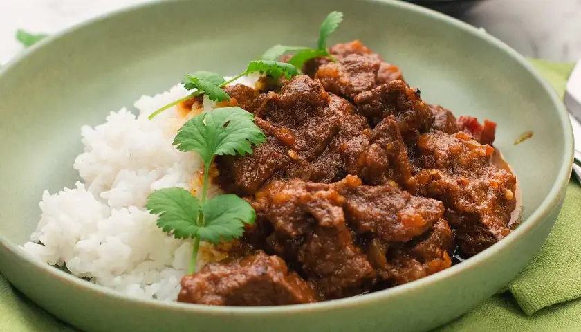 A bowl of lamb curry with rice and cilantro garnish.