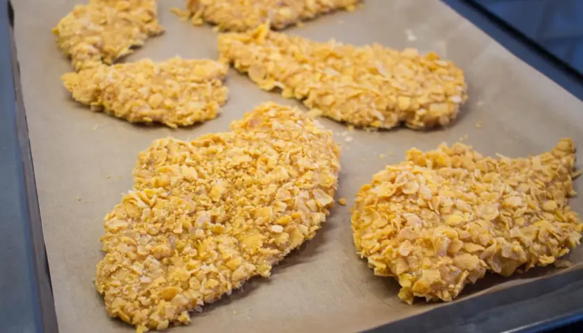 Flera bitar cornflakes kyckling ligger på en bakplåt.