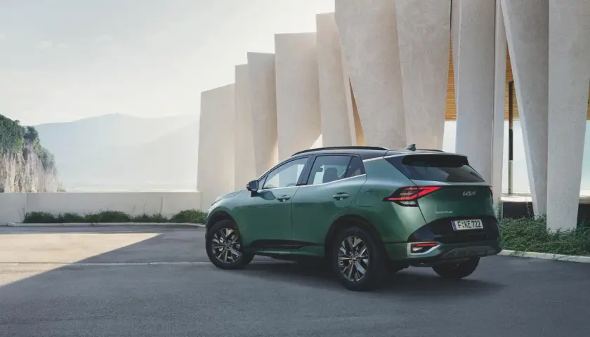 Zielony samochód Kia Sportage zaparkowany przed nowoczesnym budynkiem z elementami skalnymi w tle.