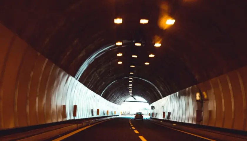 Samochód jedzie przez tunel, pokonując kolejne odległości w tunelu. Światła sufitowe oświetlają drogę.