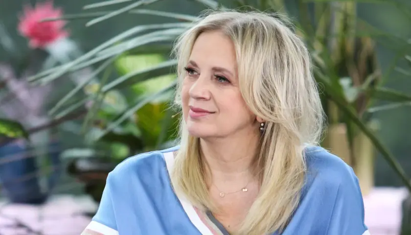 Marzena Rogalska w błękitnej bluzce z naszyjnikiem, na tle zieleni.