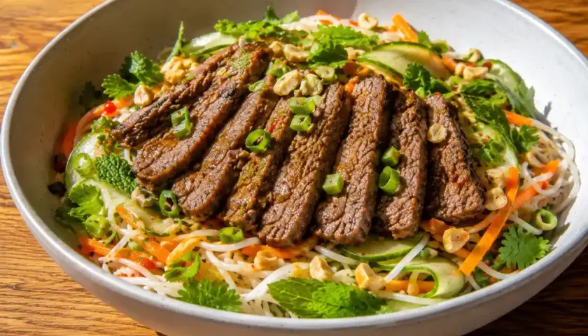 En skål med asiatisk biffsallad med nudlar, strimlad biff, gurka, morötter, mynta och jordnötter.