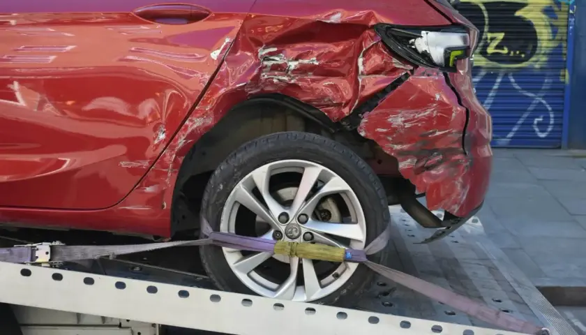 Uszkodzony czerwony samochód na lawecie, widoczna zdeformowana tylna część.