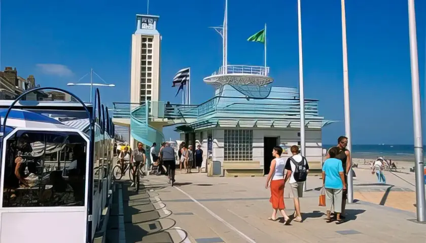 Promenade de Malo-les-Bains avec tramway, tour, bâtiments bleus et baigneurs sur la plage.