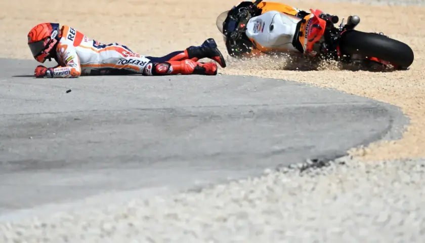 Piloto de MotoGP en el suelo tras una caída. La moto, volcada, derrapa en la grava. Un largo lap de competición que terminó mal.