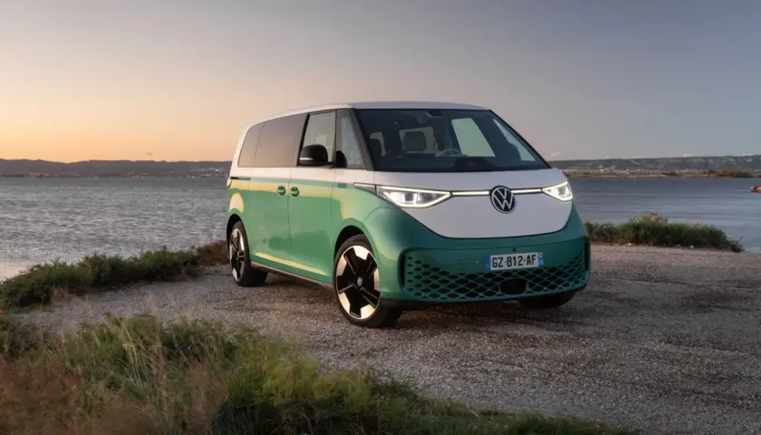 Un camping-car électrique vert et blanc, prêt pour l'aventure au bord de l'eau au coucher du soleil.