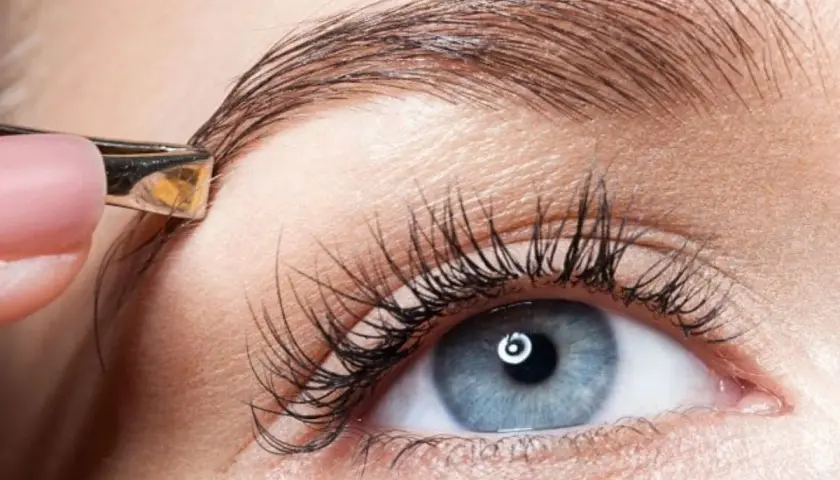 Une pince à épiler ajuste un sourcil. Un geste simple pour un dessin sourcil facile et un regard parfait.