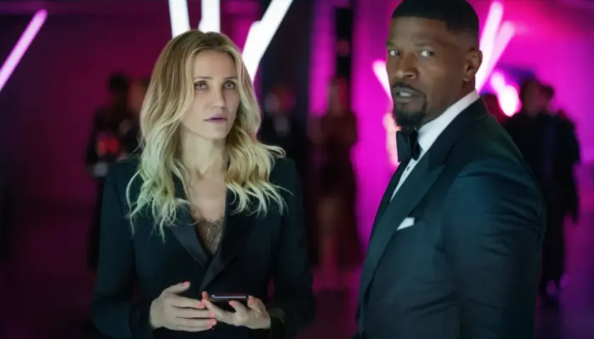 Cameron Diaz i Jamie Foxx znowu w akcji, w eleganckich strojach, na tle neonowych świateł.