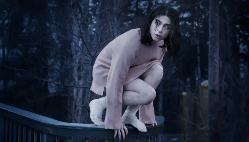 En svensk vampyr, Eli, hukar sig på ett räcke i en mörk skog.
