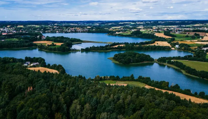 Malownicze jeziora i lasy, gdzie są Kaszuby. Widok z lotu ptaka na zielone wzgórza, pola i zabudowania.