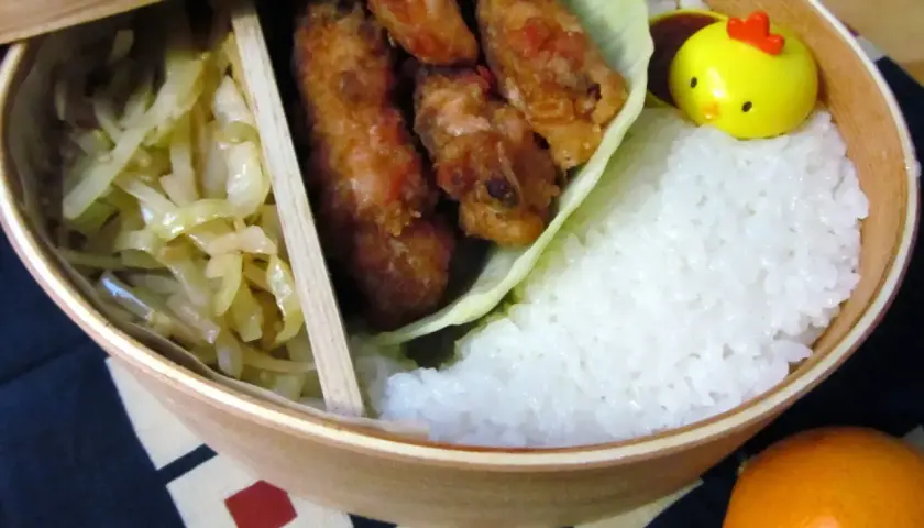 A delicious karaage bento box with crispy fried chicken, fluffy rice, pickled cabbage, and a cute chick-shaped decoration.