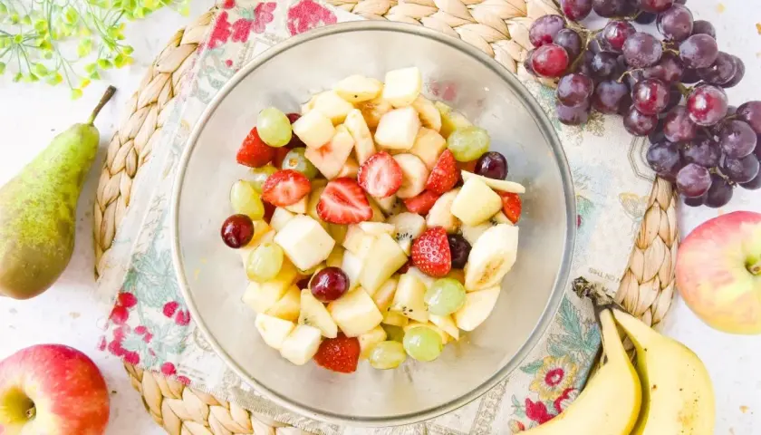 Un tazón lleno de colorida ensalada de frutas con fresas, uvas, plátano y trozos de manzana.