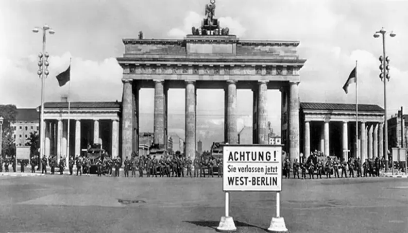 Brandenburger Tor, Soldaten und Panzer stehen Spalier. Ein Schild warnt: "ACHTUNG! Sie verlassen jetzt WEST-BERLIN". Ein Symbol des kalten Krieges.