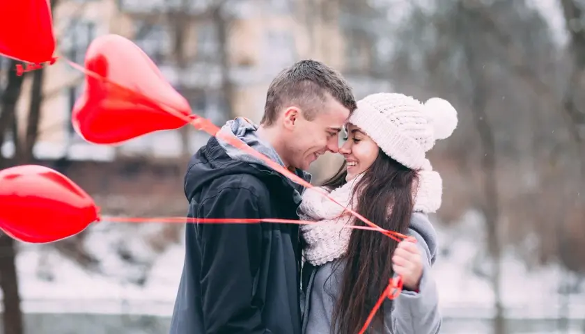 Para wzruszona, trzymająca czerwone balony w kształcie serca. Chłopak szepcze jej do ucha, co napisać dziewczynie żeby się wzruszyła.