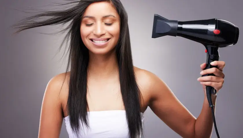 Mujer sonríe mientras se seca el pelo fino y escaso con un secador negro.
