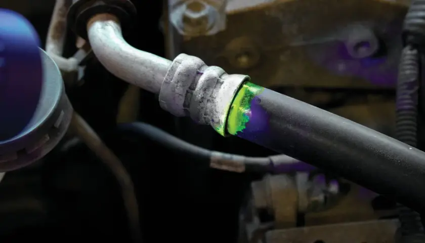 Detectando una fuga de aire en el sistema de aire acondicionado con tinte fluorescente verde y luz ultravioleta.