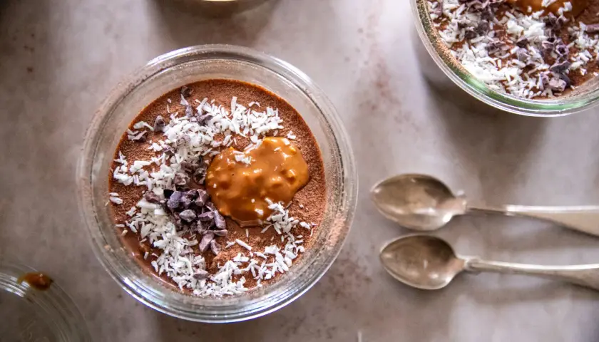 Chokladmousse med kokosflingor och kakaonibs, en härlig vegansk frukost. Två skedar ligger bredvid.