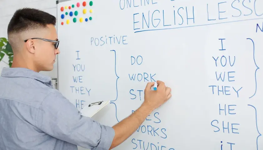 Chłopak pisze na tablicy "ONLINE ENGLISH LESSON". Uczy się, ile jest słów w języku angielskim, tworząc zdania.