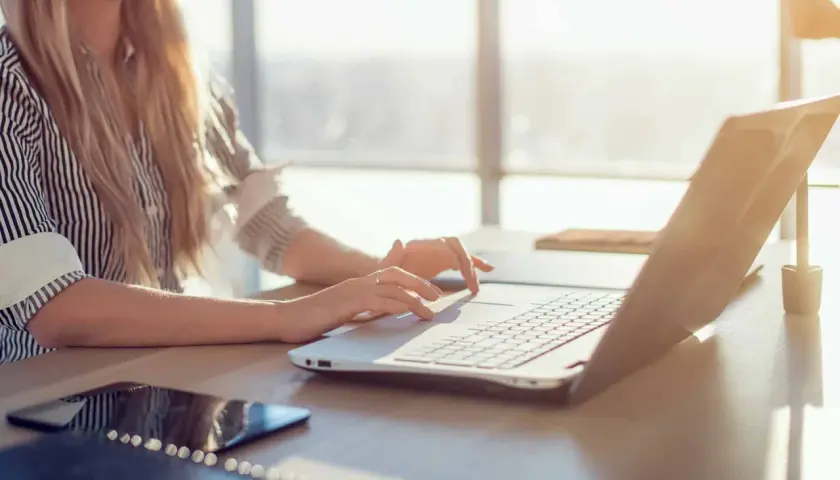 Kobieta z blond włosami pracuje na laptopie w słoneczny dzień.