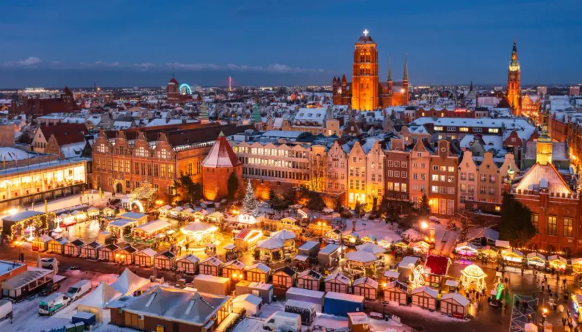 Gdańsk jarmark świąteczny nocą, z oświetlonymi kramami, karuzelą i zabytkową zabudową w tle.