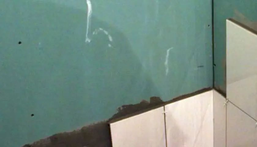 Angolo di una stanza con piastrelle su cartongesso in fase di posa. La parete verde è pronta per essere rivestita.