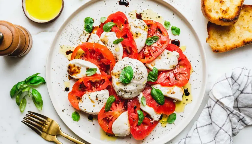 Caprese-Salat mit frischen Tomaten, veganem Mozzarella und Basilikum, beträufelt mit Olivenöl und Balsamico. Dazu geröstetes Brot.