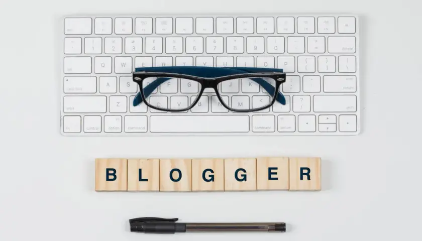 Klawiatura, okulary i drewniane klocki z napisem "BLOGGER".