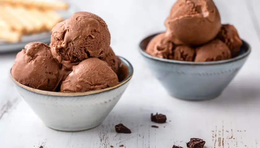 Due ciotole piene di cremoso gelato al cioccolato, con pezzi di cioccolato sparsi sul tavolo.