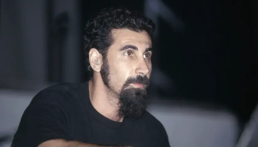 Serj Tankian, wokalista System of a Down, z charakterystyczną brodą i słuchawką w uchu, gotowy do wykonania kolejnych energetycznych utworów.
