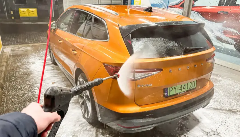Jak dobrze umyć auto na myjni bezdotykowej? Pomarańczowa Skoda Enyaq jest spryskiwana wodą pod ciśnieniem.